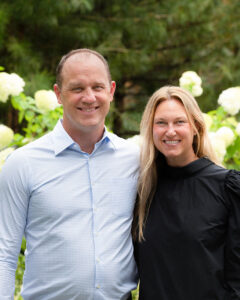 David and Ashley Skatoff P’25 are standing outside in front of a flowering shrub.